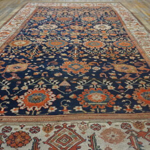 Navy area rug with orange floral motifs and a wide cream border sits on light wood planks.