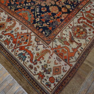 Detailed corner of a navy and rust patterned rug with a cream border on distressed gray wooden floors.