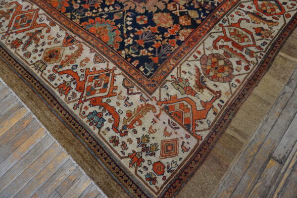 Detailed corner of a navy and rust patterned rug with a cream border on distressed gray wooden floors.