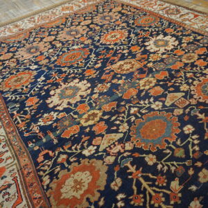 Dark blue traditional rug with rust orange and ivory floral motifs and a light border on wood flooring.