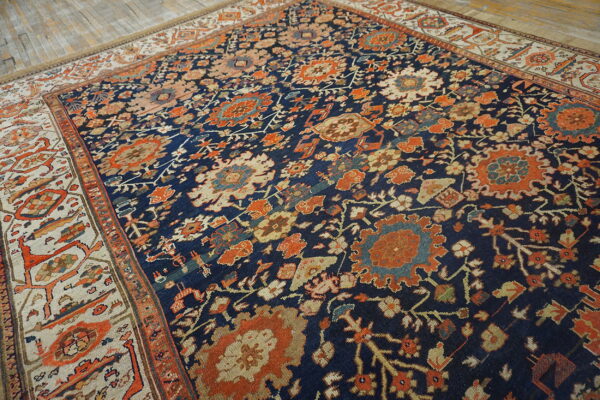 Dark blue traditional rug with rust orange and ivory floral motifs and a light border on wood flooring.