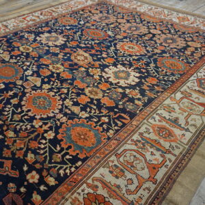 Blue rug with dense orange floral pattern and a geometric cream border on distressed wood flooring.