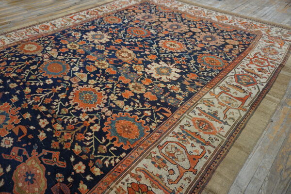 Blue rug with dense orange floral pattern and a geometric cream border on distressed wood flooring.