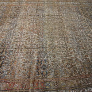 Large distressed traditional rug featuring an elaborate all-over pattern in shades of taupe, rust, and navy blue.