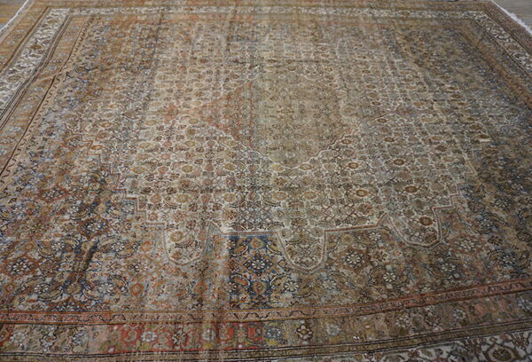 Large distressed traditional rug featuring an elaborate all-over pattern in shades of taupe, rust, and navy blue.