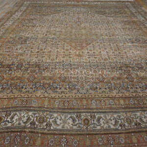 Low-pile ornamental rug in earth tones and cream displayed fully on wide brown hardwood floors.
