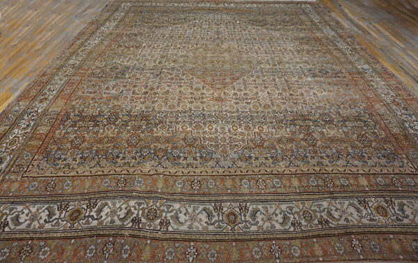 Low-pile ornamental rug in earth tones and cream displayed fully on wide brown hardwood floors.