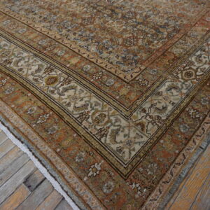A traditional rug corner featuring rust, cream, blue, and gold floral patterns rests on distressed wood flooring.