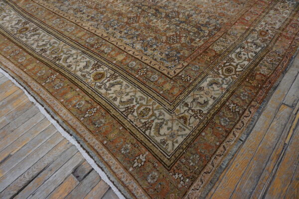 A traditional rug corner featuring rust, cream, blue, and gold floral patterns rests on distressed wood flooring.