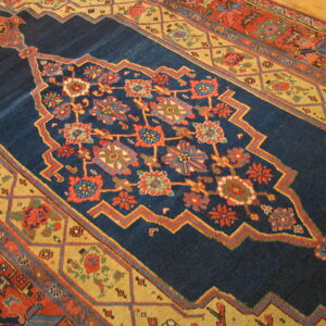 Richly colored blue rug featuring stylized red and gold floral geometric patterns on a wood floor.