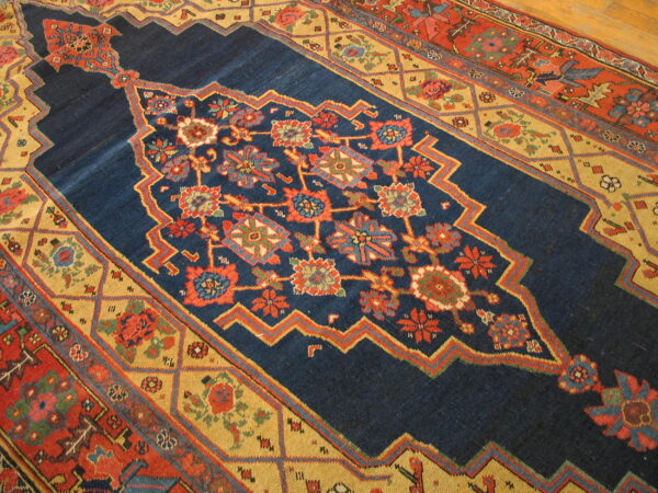Richly colored blue rug featuring stylized red and gold floral geometric patterns on a wood floor.