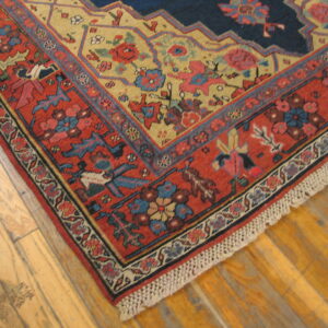 Low-pile rug corner featuring navy, gold, and terracotta colors with intricate borders on light wood floorboards.