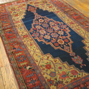 Red and gold patterned rug with a deep blue medallion rests on wide plank hardwood floor.