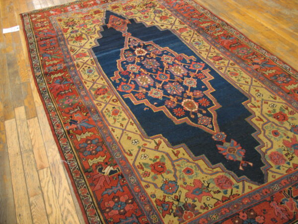 Red and gold patterned rug with a deep blue medallion rests on wide plank hardwood floor.