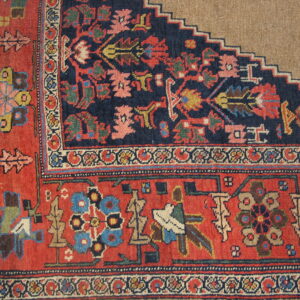 Navy and red patterned rug corner with complex borders meets a flat beige surface with a stepped edge.