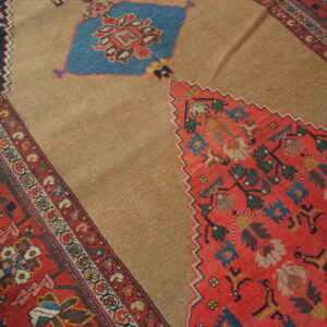 Traditional rug detail showing a camel-colored field contrasting with serrated red, blue, and multi-colored geometric motifs.