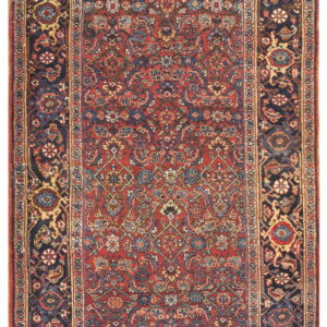 A narrow runner rug features a deep red, dense floral field surrounded by a wide navy patterned border.