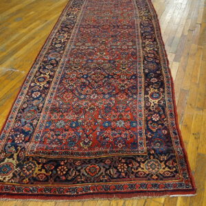 Red and navy traditional runner rug with dense patterns lies on distressed golden hardwood floor.