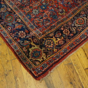 Close-up of a low-pile red and navy floral patterned rug on rustic wooden floorboards.