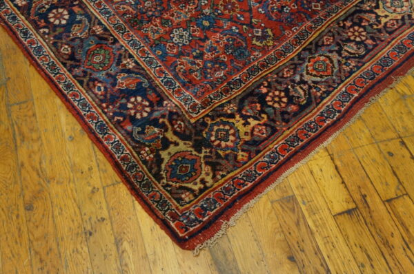 Close-up of a low-pile red and navy floral patterned rug on rustic wooden floorboards.