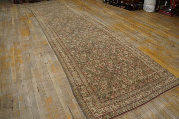 Muted olive green runner rug with pink and cream patterns displayed on distressed plank wood flooring.
