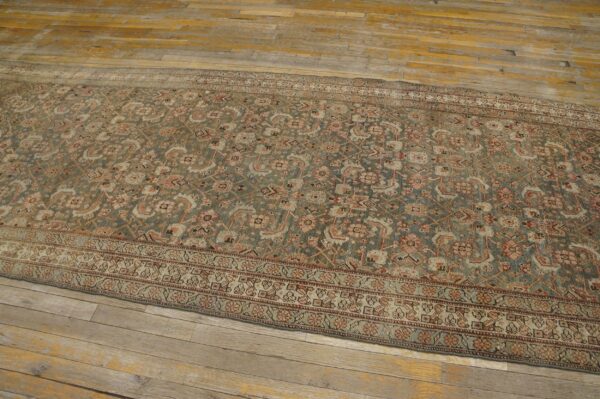 Muted runner rug with intricate floral designs in sage, rust, and cream on old wood planks.