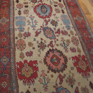 Rust and beige rug with large pink and blue abstract motifs on exposed hardwood flooring.