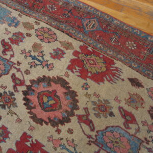 Close-up of a rug with a beige field, red border, and stylized blue, pink, and red floral motifs on wood floor.