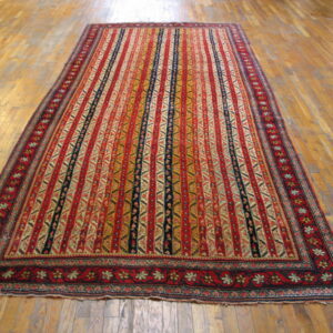 This low-pile rug features dense vertical stripes of red, gold, and dark blue on wood floors.