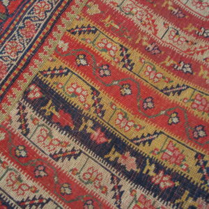 Intricate border pattern in red, navy, gold, and white with tightly woven low-pile texture.