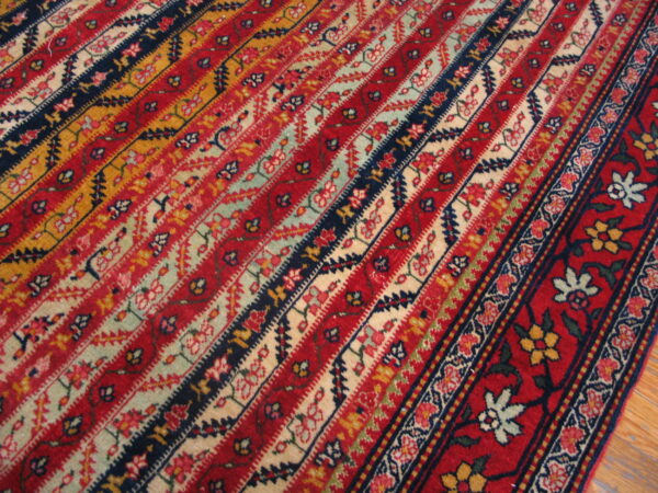 Close detail of a striped rug with red, navy, gold, and pale floral bands next to a red border.