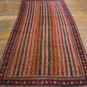 Red, gold, and navy striped rug with intricate geometric motifs displayed on worn wood plank flooring.