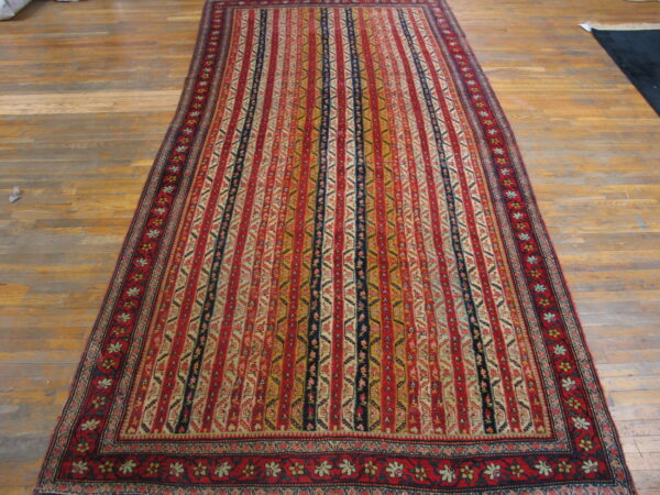 Red, gold, and navy striped rug with intricate geometric motifs displayed on worn wood plank flooring.