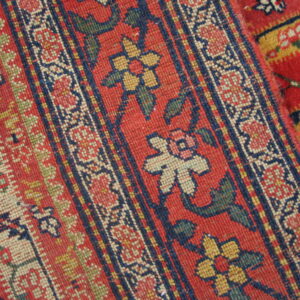 Red rug detail showing dense, low-pile, striped patterns in navy, cream, yellow, and green.