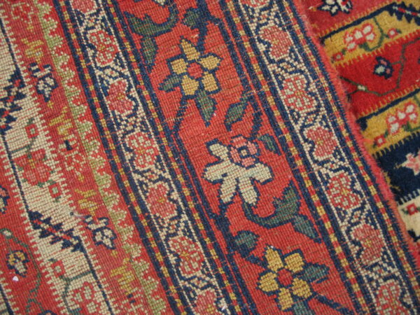 Red rug detail showing dense, low-pile, striped patterns in navy, cream, yellow, and green.