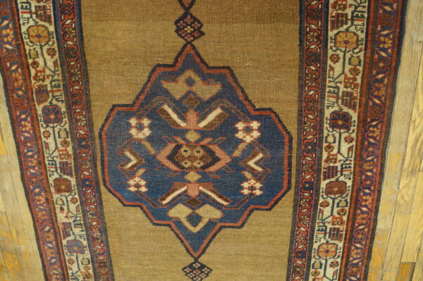 Elongated runner with a tan field, deep blue center medallion, and multi-banded red and cream borders on wood floor.