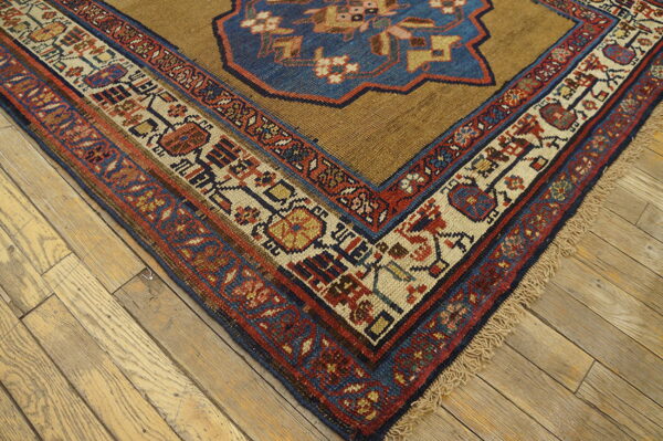 Tan rug corner with complex red, blue, and cream geometric borders on light wood plank flooring.