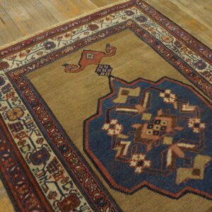 A tan rug with a large indigo blue medallion and geometric borders rests on worn wooden flooring.