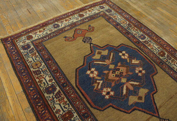 A tan rug with a large indigo blue medallion and geometric borders rests on worn wooden flooring.