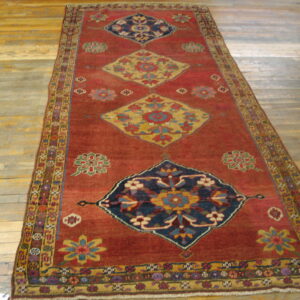 Rust runner rug with repeating blue and gold medallions and floral motifs rests on worn hardwood flooring.