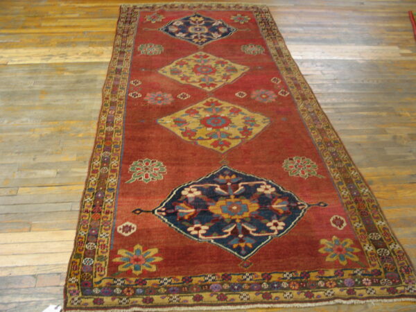 Rust runner rug with repeating blue and gold medallions and floral motifs rests on worn hardwood flooring.