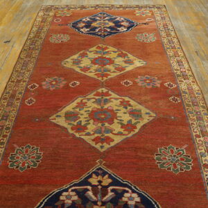 Low pile runner with red, navy, and gold diamond medallions centers a distressed wood floor with golden tones.