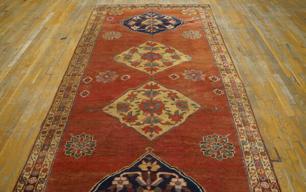 Low pile runner with red, navy, and gold diamond medallions centers a distressed wood floor with golden tones.