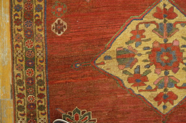 Red rug detail shows a large golden yellow medallion and multicolored geometric border on distressed wood planks.