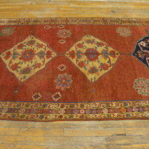 Rust-colored rug featuring repeating yellow and blue patterned diamonds lies on light wooden flooring.