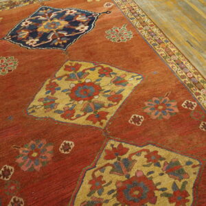 Rust-red rug with floral medallions and a patterned border rests on distressed yellow wood planks.