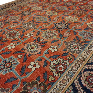 Rust red rug featuring an all-over traditional floral vine pattern in blue, navy, cream, and yellow.