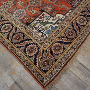 Ornate traditional rug with rust field and navy blue border resting on distressed gray wood flooring.