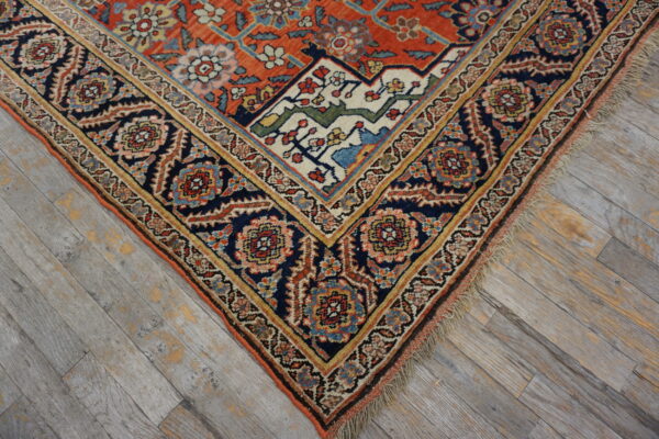 Ornate traditional rug with rust field and navy blue border resting on distressed gray wood flooring.