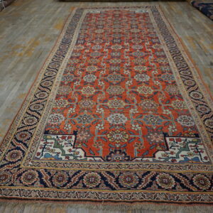 Orange runner rug with an all-over multicolor floral pattern and wide navy borders on distressed wood.